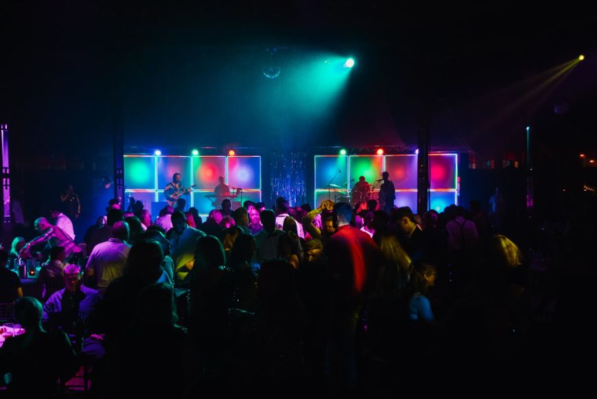 a crowd of people in a dark room, with colourful lights all around